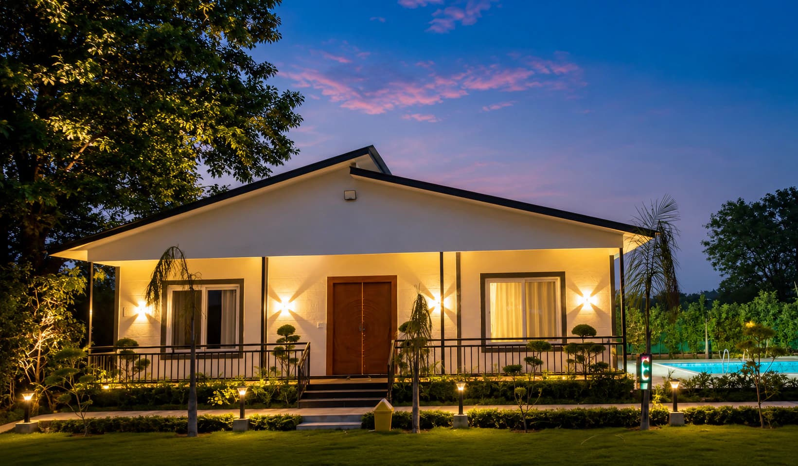 The estate residence at twilight, with warm façade lighting, landscaped hedges and the pool beyond